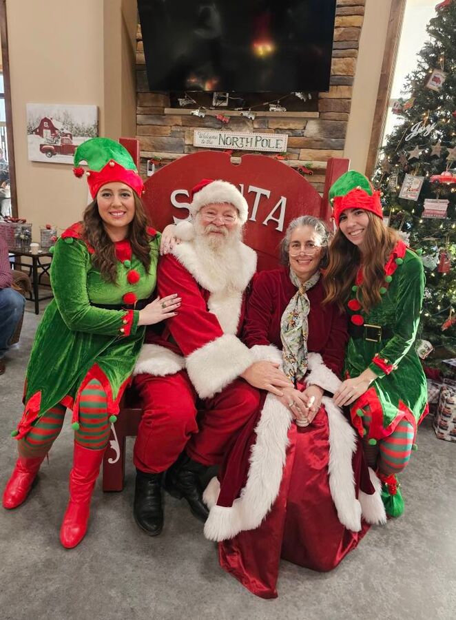 Santa and Mrs. Claus sitting together with two of their elves